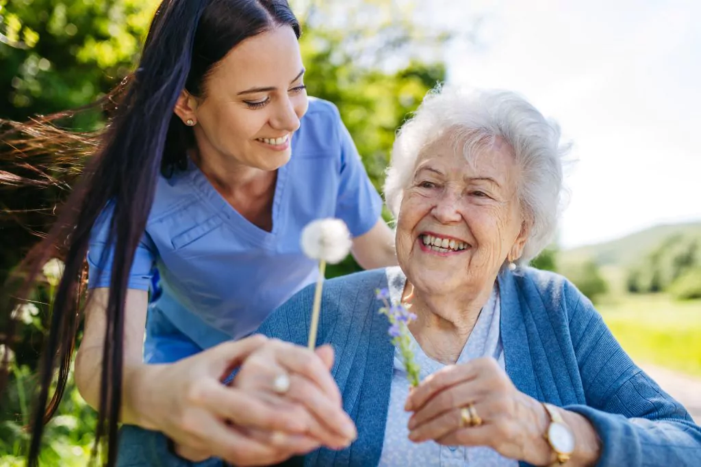 Female,Caregiver,And,Senior,Woman,In,Wheelchair,Holding,Dandelion,,Picking